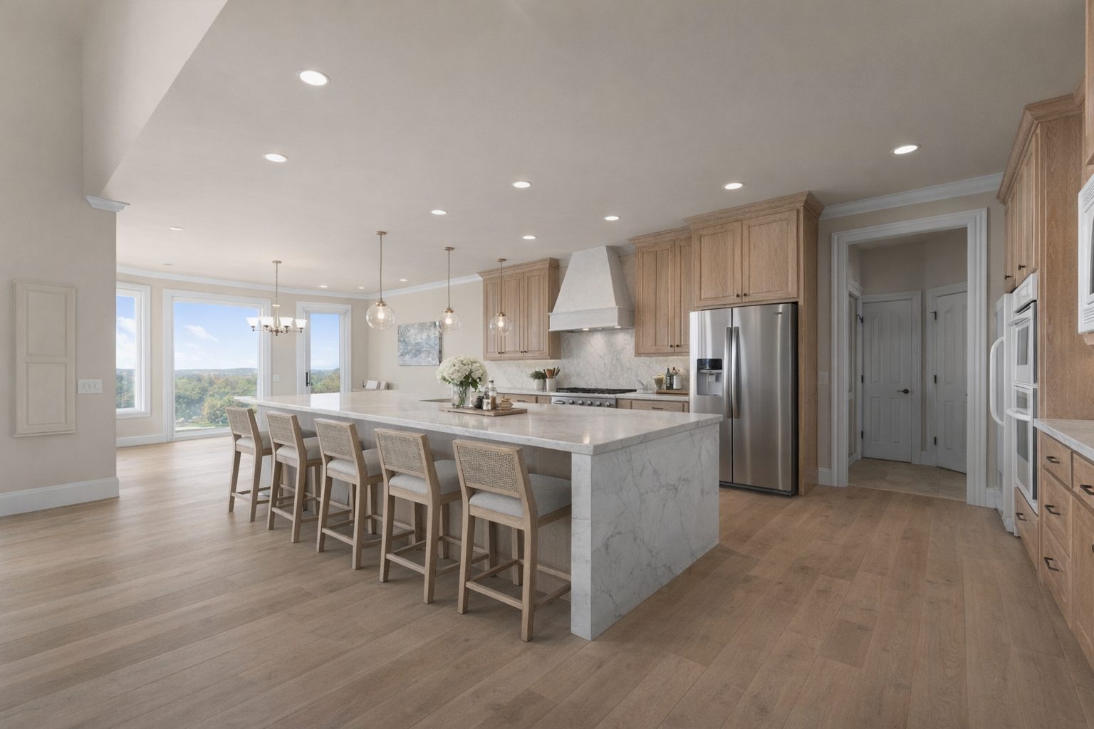 Bright luxury kitchen with a marble waterfall island, light oak cabinetry, cane barstools, and a wall of windows overlooking green hills.