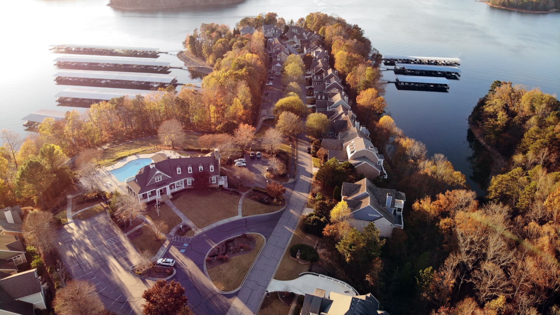 Aerial view of Harbour Point on Lake Lanier at golden hour: waterfront homes, covered marina docks, and the clubhouse pool among autumn trees.